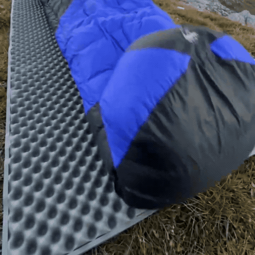 Blue sleeping bag unrolled on a campsite sleeping mat